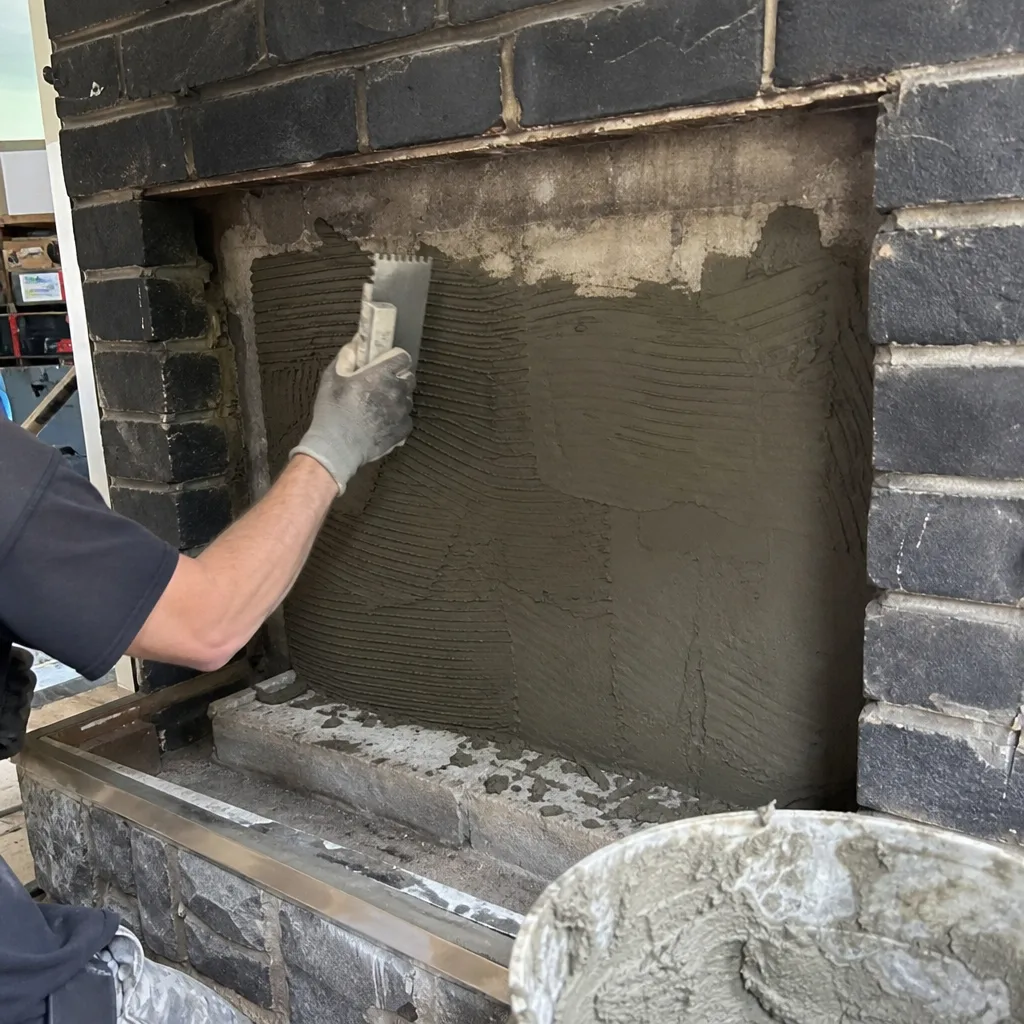 Tradesperson applying mortar with a notched trowel to a fireplace